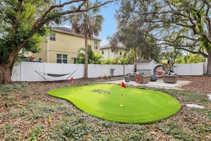 Un jardin avec un green d’entraînement au golf, un hamac et du mobilier d’extérieur.