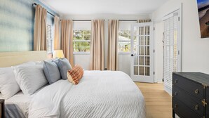 Un dormitorio con cama, cortinas, cómoda y puerta que da a un balcón.