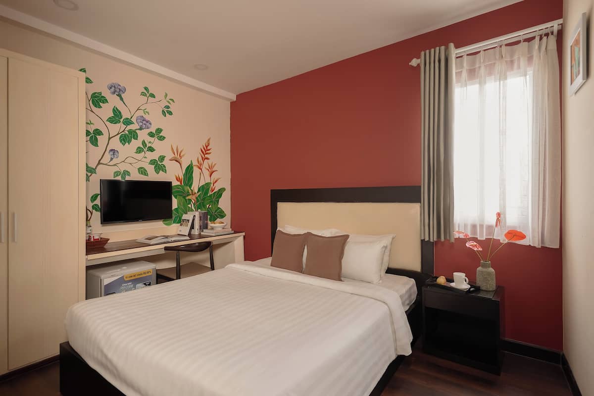 Une chambre d’hôtel avec un lit, un bureau doté d’un téléviseur à écran plat, une petite table avec un vase et une fenêtre avec des rideaux.
