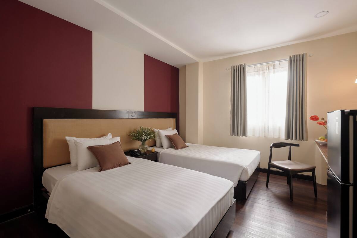 Une chambre d’hôtel avec deux lits, une chaise, un bureau et un réfrigérateur.