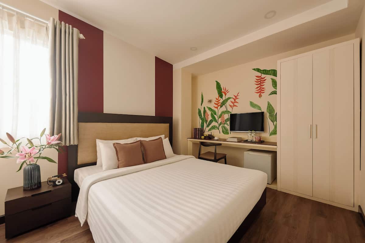 Une chambre d’hôtel équipée d’un lit, d’un bureau, d’une télévision, d’une armoire et d’un mur décoré de plantes.