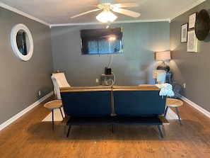 A living room with a dark blue sofa, a ceiling fan, a flat-screen TV, a round mirror, and a small side table. - Beautiful 3Beds in Bridge City! (Bridge City)