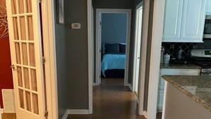 A hallway with wooden flooring leading to a bedroom with a bed and a bathroom with a toilet and sink. - Beautiful 3Beds in Bridge City! (Bridge City)