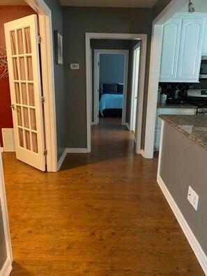 A hallway with wooden flooring leading to a bedroom with a bed and a bathroom with a toilet and sink. - Beautiful 3Beds in Bridge City! (Bridge City)