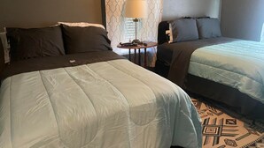 A hotel room with two beds, a small table with a lamp, and patterned curtains. - Beautiful 3Beds in Bridge City! (Bridge City)