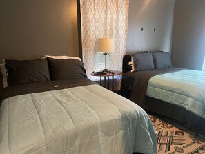 A hotel room with two beds, a small table with a lamp, and patterned curtains. - Beautiful 3Beds in Bridge City! (Bridge City)