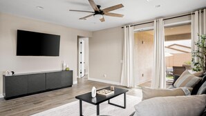 A modern living room with a flat-screen TV, a dark wood cabinet, a black coffee table, and a grey sofa. - 3 BR home w/Pool & Game room (Phoenix)