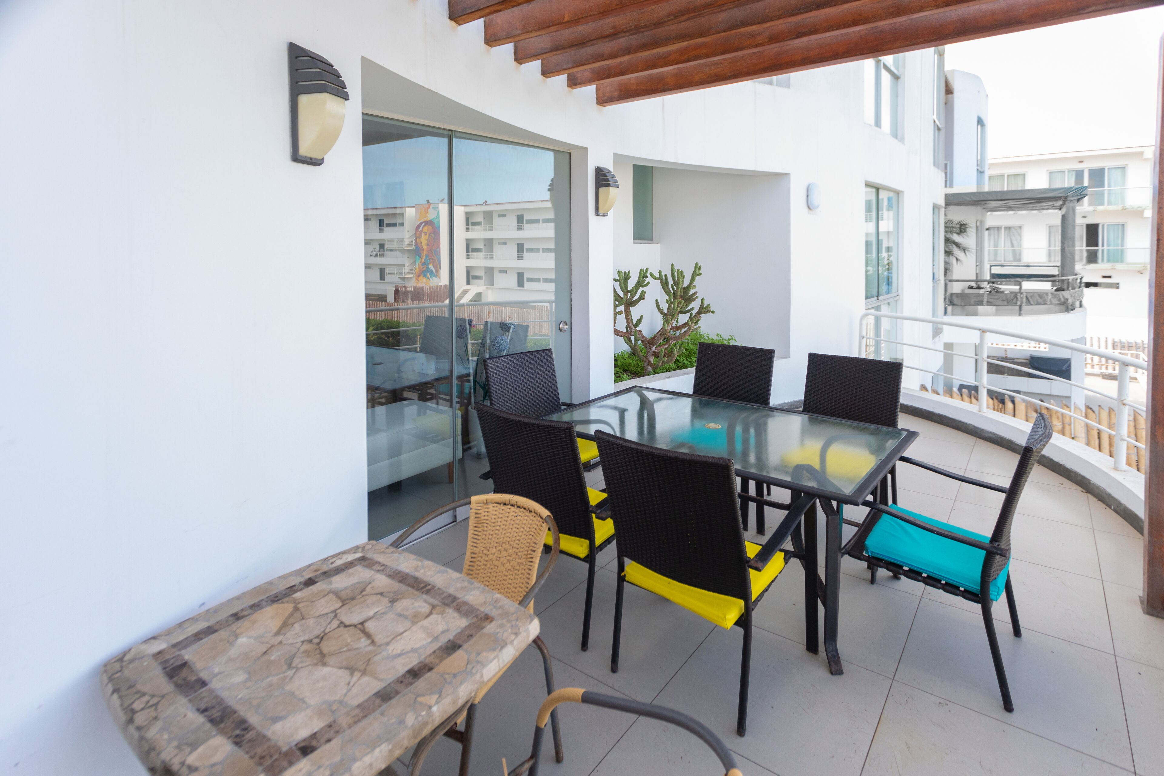 Un espacio de comedor moderno al aire libre, con una mesa y sillas de vidrio, una pequeña mesa de madera y vistas a la ciudad.