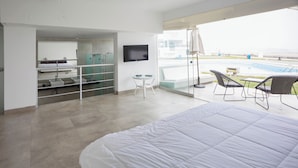 A modern hotel room with a large bed, a TV, a small table, and a balcony with a pool view.