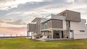 A modern two-story house with a pool, large windows, and a view of the ocean.