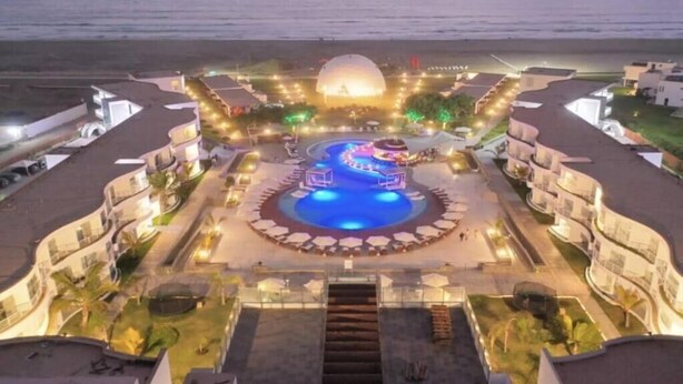 A resort with a central pool, multiple balconies, and a view of the ocean.