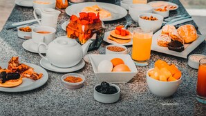 A breakfast table with various food items and drinks, overlooking a swimming pool with umbrellas.