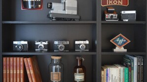 A bookshelf with vintage cameras, a bottle, and books.