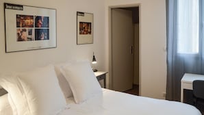 A hotel room with a large bed, a desk, and two framed pictures on the wall.