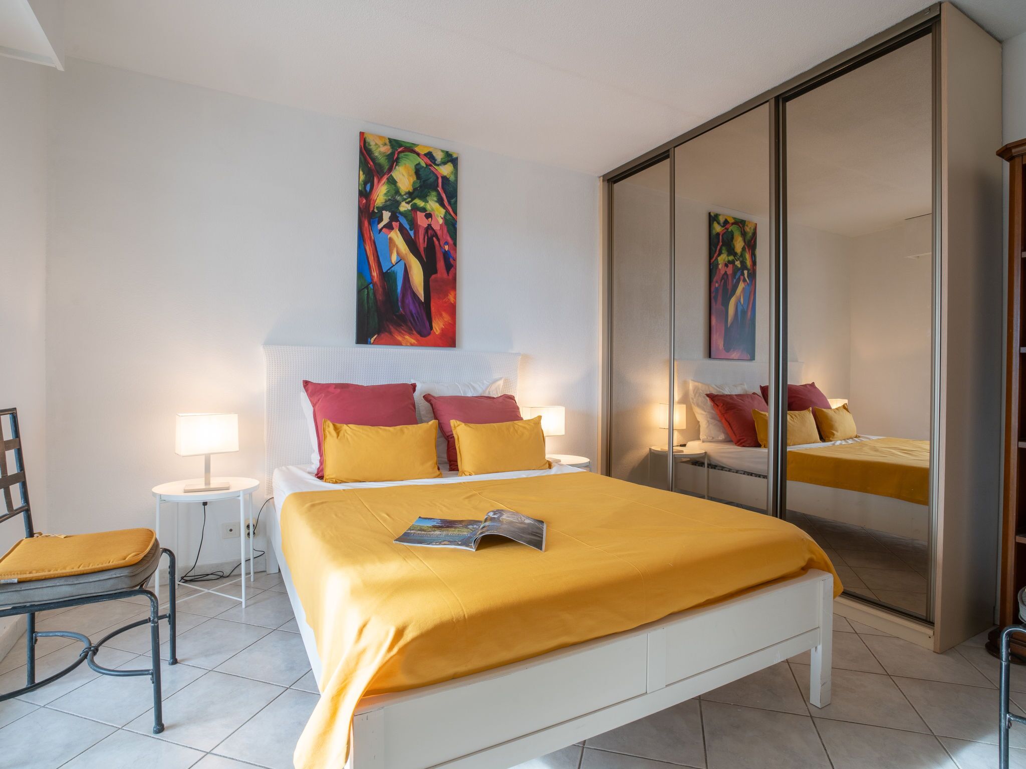 A modern bedroom with a large bed, two bedside tables, a chair, and a wardrobe.