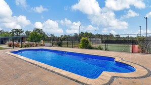 A rectangular swimming pool with a tiled deck surrounding it, a fence, and a clear sky with clouds.