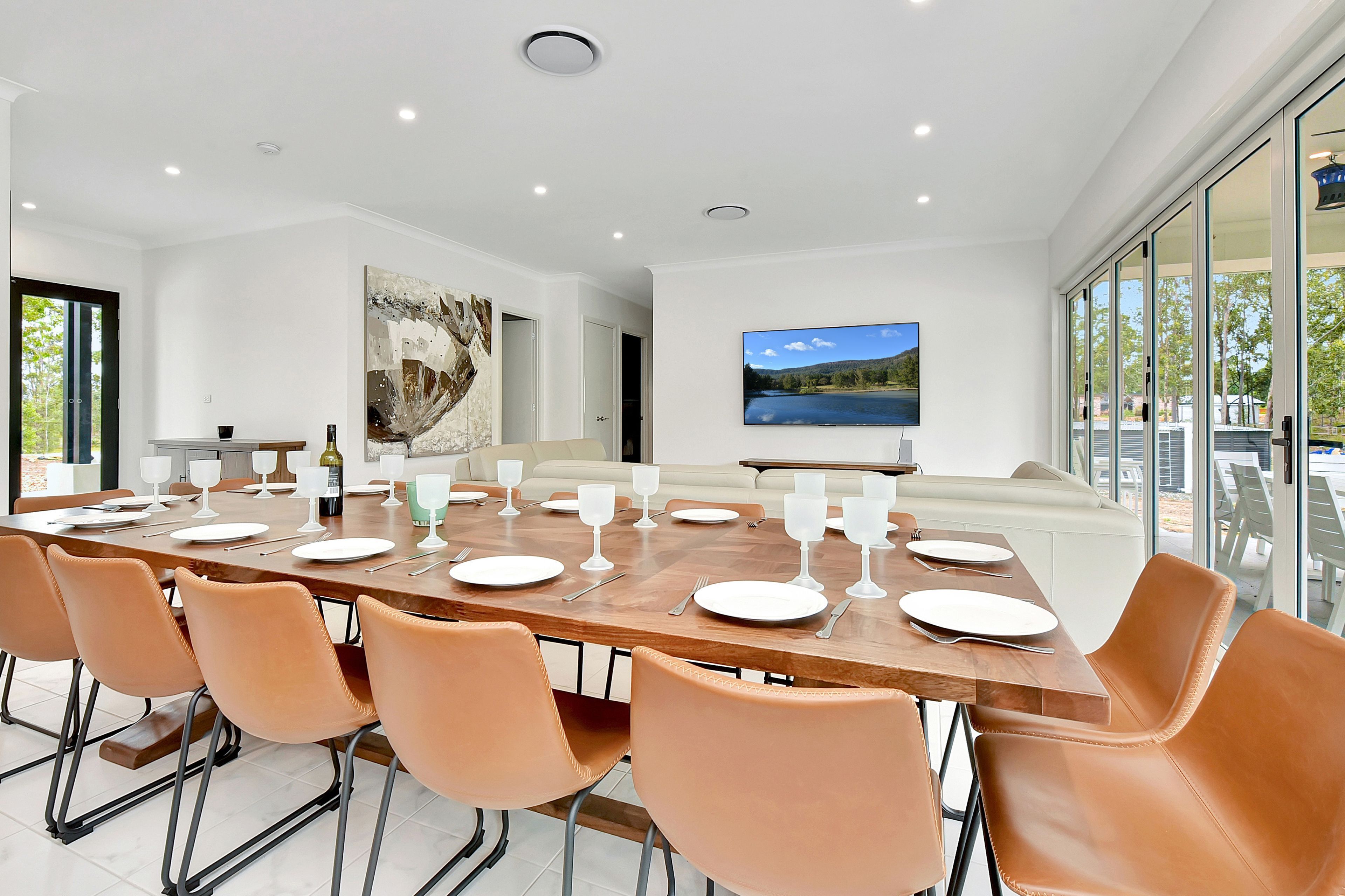 Uma sala de jantar moderna com uma mesa grande posta para refeição, cercada por cadeiras de couro.