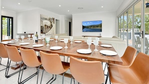 A modern dining room with a large table set for a meal, surrounded by leather chairs.