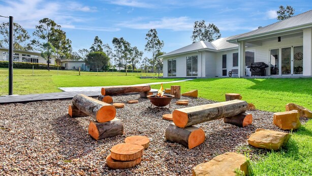 A residential property with a landscaped outdoor area featuring a fire pit surrounded by logs and stones.