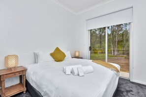 A bedroom with a large bed, a nightstand, a lamp, and a view of the outdoors.
