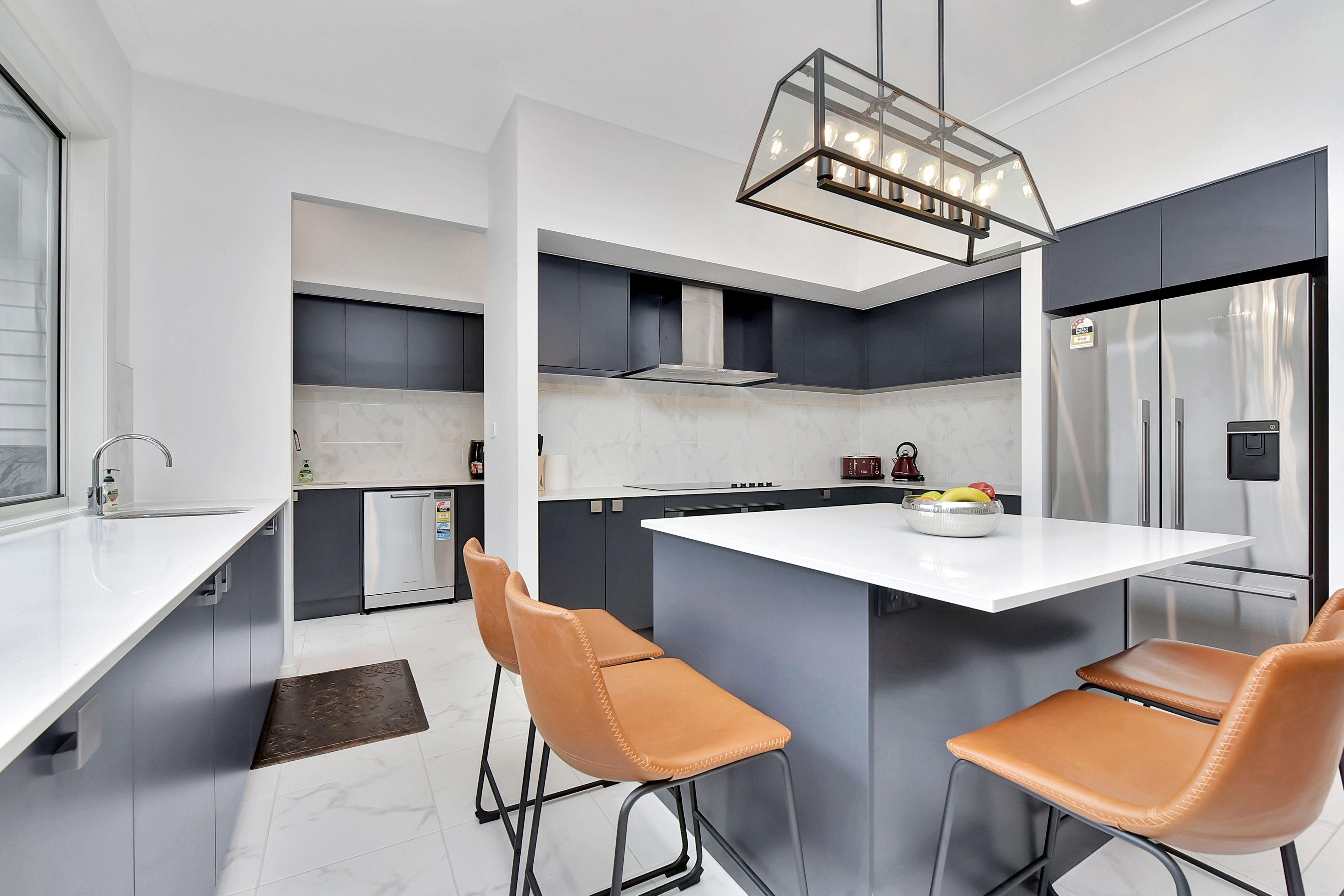 Una cocina moderna con una isla central, taburetes de bar, horno empotrado y refrigerador de acero inoxidable.