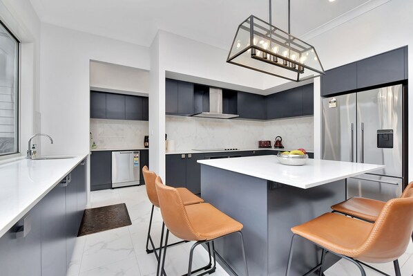 A modern kitchen with a central island, bar stools, a built-in oven, and a stainless steel refrigerator.