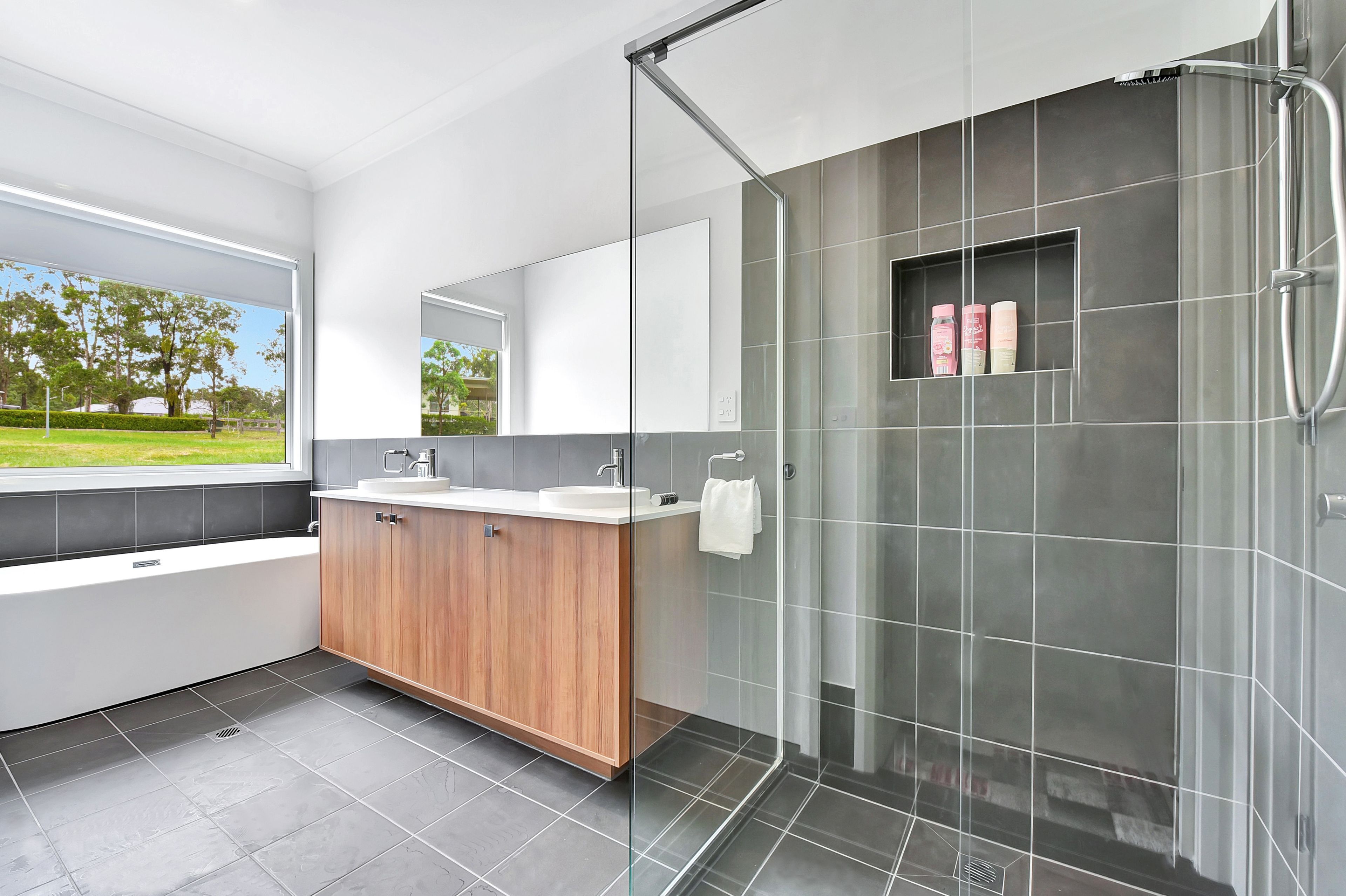 A modern bathroom with a glass shower enclosure, a large mirror, and a view of the outdoors.
