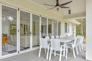 A covered patio with a table and chairs, large sliding glass doors, and a ceiling fan.