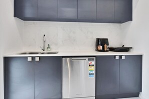 Een compacte keuken met een vaatwasser, een koffiezetapparaat en een spoelbak.