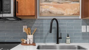 A kitchen with a stainless steel sink, wooden cabinets, a microwave, and a painting above the sink. - Golden Hour - A Southside Home (Chattanooga)