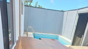 Mesa de madeira ao ar livre com bancos, piscina e porta de correr de vidro.