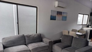 Uma sala de estar moderna com sofás cinza, um espaço de jantar e uma cozinha.