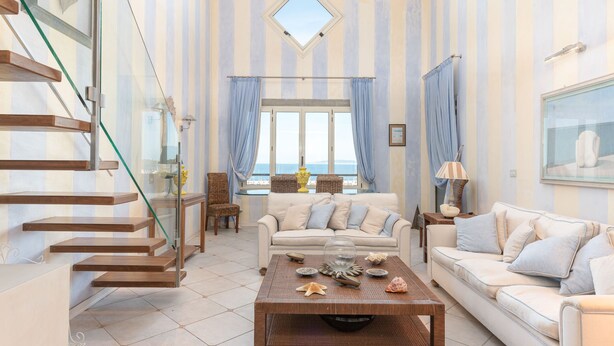 Ein geräumiges Wohnzimmer mit moderner Wendeltreppe, einem großen Fenster mit Meerblick und einer gemütlichen Sitzecke mit Couchtisch.