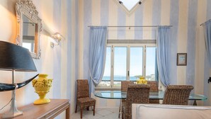 Ein Zimmer mit Streifenmuster-Tapete, einem großen Fenster mit Vorhängen, Korbmöbeln und Meerblick.
