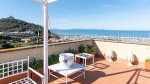 Eine Terrasse mit einem weißen Tisch, einem großen weißen Blumentopf und Blick auf das Meer und den Hafen.