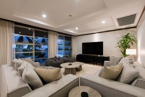 A modern living room with a sofa set, a coffee table, a flat-screen TV, and a large window with curtains. - Katamanda Villa Aliya Jacuzzi Pool near Kata Beach (Karon)