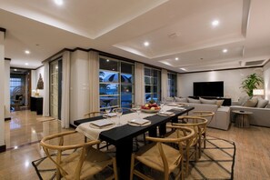 A modern dining area with a long table, multiple chairs, and a view through large windows. - Katamanda Villa Aliya Jacuzzi Pool near Kata Beach (Karon)