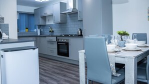 A modern kitchen with grey cabinets, a built-in oven, and a dining area with a table set for four. - Impeccable 4-Bed House in Telford, West Midlands (Telford)