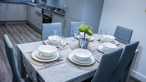 A modern dining area with a rectangular table set for four, surrounded by blue upholstered chairs. - Impeccable 4-Bed House in Telford, West Midlands (Telford)