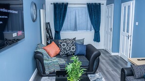 A living room with a black sofa, a coffee table with a plant, and a TV mounted on the wall. - Impeccable 4-Bed House in Telford, West Midlands (Telford)