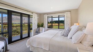 Une chambre avec un grand lit, une chaise et une vue sur un paysage montagneux, visible à travers une porte-fenêtre coulissante.