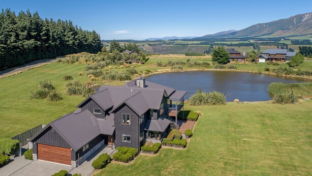 Une grande maison moderne avec un garage, entourée d’une pelouse bien entretenue et d’un lac.