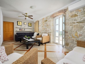 A living room with a stone wall, a ceiling fan, a sofa, a wicker chair, a coffee table, and a door.