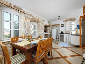 A dining area with a stone wall, wooden furniture, and a kitchen with a refrigerator and sink.