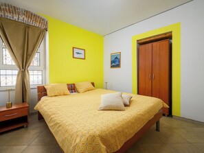 A bedroom with a bed, curtains, a wooden wardrobe, and two framed pictures on the wall.