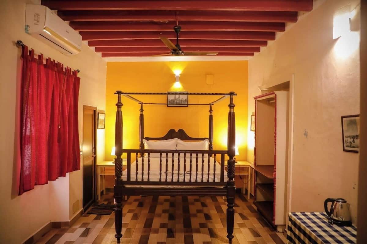 A room with a four-poster bed, a ceiling fan, a red curtain, and a checkered tablecloth on a small table.