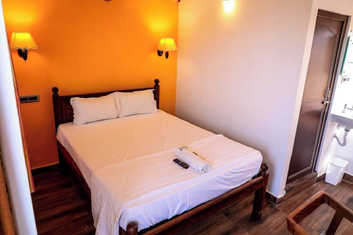 A bedroom with a wooden bed, white linens, two wall-mounted lamps, and a small wooden stool.