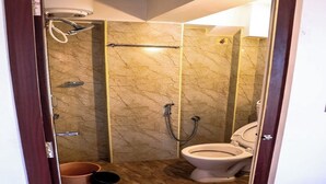 A compact bathroom with a toilet, a shower, and a marble-tiled wall. - The French Villa (Puducherry)