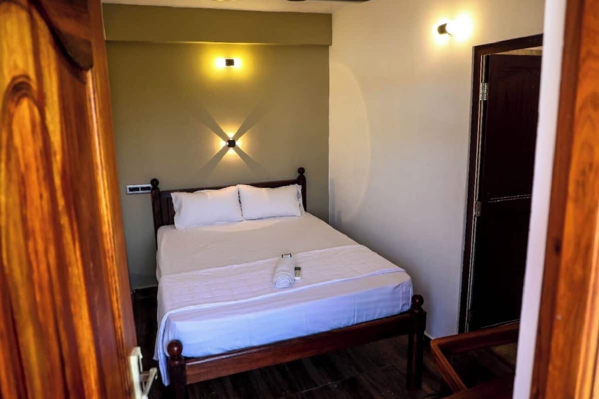 A neatly made bed in a room with a wooden headboard, a ceiling fan, and a wall-mounted light fixture.