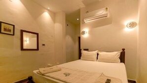 A hotel room with a neatly made bed, a bedside table, a wall-mounted air conditioner, and a framed picture on the wall. - The French Villa (Puducherry)